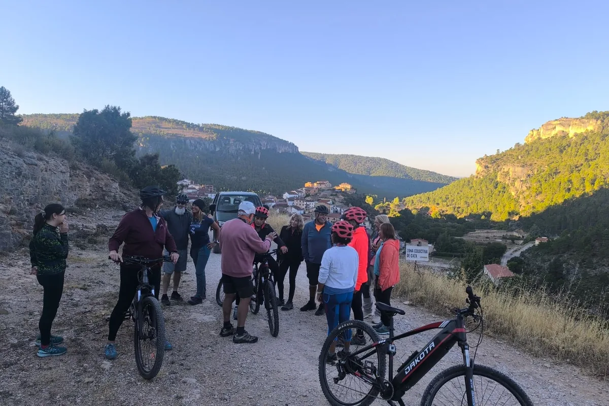 Grupo de participantes con bicicletas eléctricas en una pista de tierra, con un pueblo y el valle al fondo