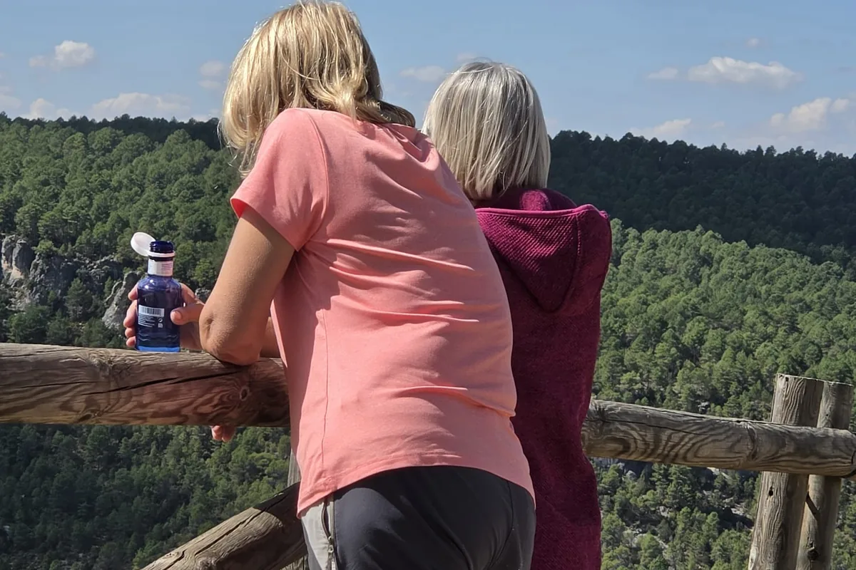Dos mujeres apoyadas en una barandilla de madera mirando el pinar