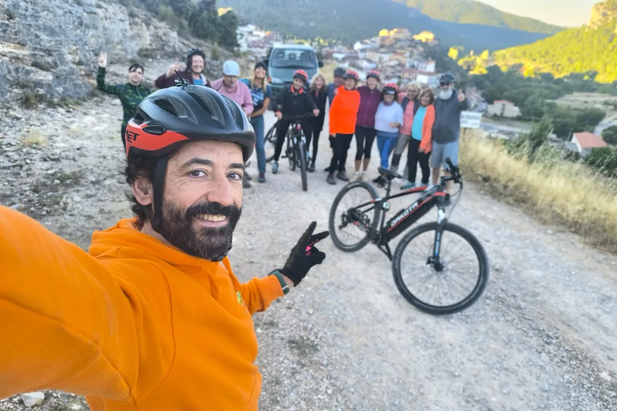 Hombre con casco y sudadera naranja se hace un selfi con el grupo y las bicicletas detrás